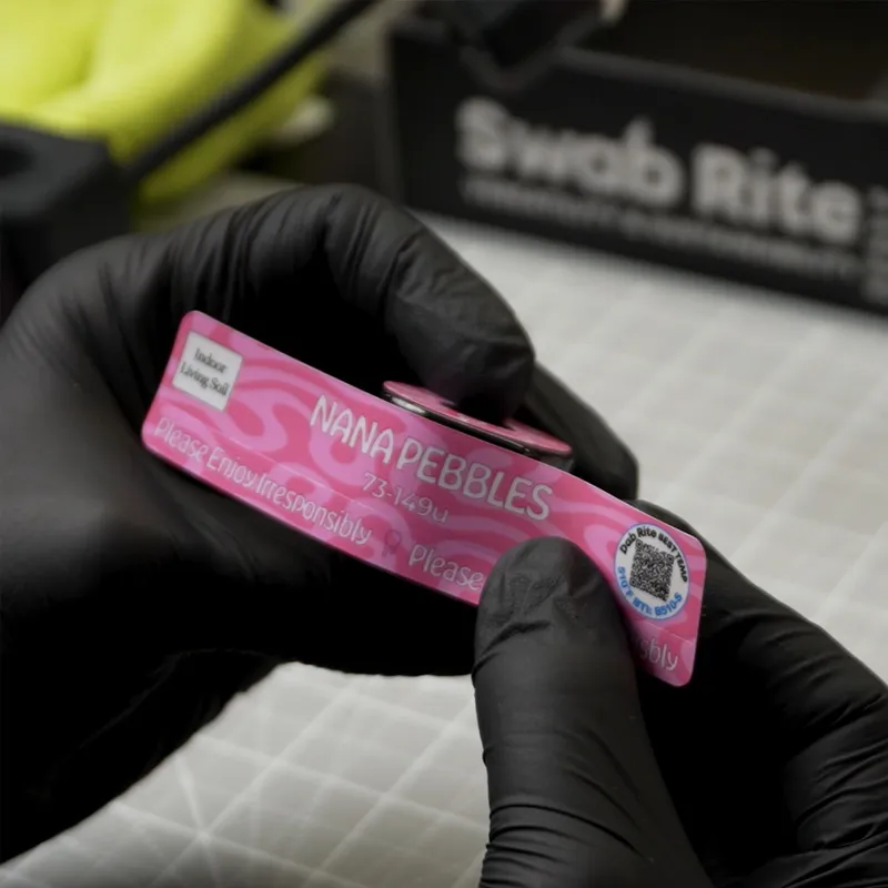 Gloved hand holding a pink QR product label